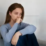 Joven con un bajón emocional, sentada en un sofá, con la mano en la boca y la mirada perdida.