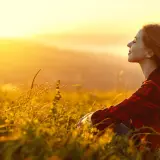 Mujer sonríe en un campo al atardecer, disfrutando de la paz y fortaleciendo su autoestima personal.