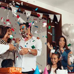 Familia celebrando fiestas sorpresa con confeti y globos. Todos ríen y se abrazan, creando un ambiente de alegría.