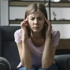 Mujer sentada en un sillón, con los ojos cerrados y las manos en las sienes, parece estar comiéndose la cabeza por algo.