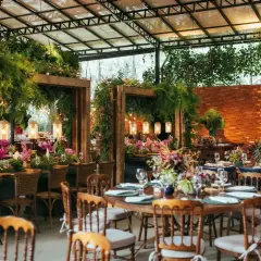 Salón de eventos decorado con abundante vegetación, flores y luces cálidas, con mesas puestas para una celebración.