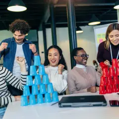 Equipo celebrando en juegos de empresa, apilando vasos de colores.