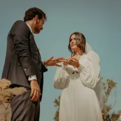 Novios intercambian anillos en una boda civil informal al aire libre. Un vestido blanco y un traje oscuro, rodeados de naturaleza.