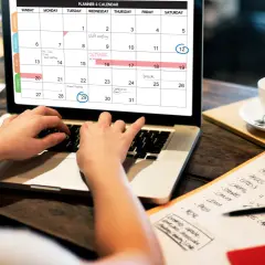 Persona organiza su **curso gestión administrativa** en un calendario digital, con una taza de café al lado.