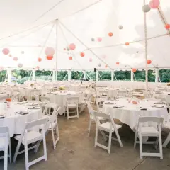 Carpa blanca con mesas redondas y sillas blancas, decorada con farolillos de colores. Un espacio ideal para **sitios de eventos**.