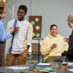 Celebración en el workshop de la empresa. Cuatro colegas brindan con copas de champán, sonriendo y charlando animadamente.