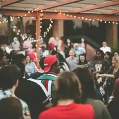 Grupo de personas disfrutando en una fiesta al aire libre, con luces decorativas. ¡Excelentes ideas para cenas de empresa!
