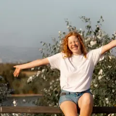 Chica pelirroja sonríe con brazos abiertos, disfrutando de la vida. Un símbolo de autoayuda y autoestima en armonía con la naturaleza.