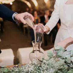 Manos de novios vierten arena en un jarrón, simbolizando su unión en una boda simbólica.
