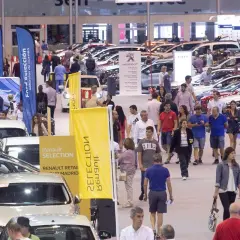 Gente paseando entre coches en una feria comercial. Banderolas de Ford y Renault anuncian vehículos de ocasión.