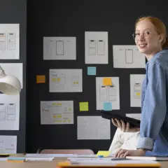 Joven sonríe mientras revisa wireframes de apps, preparándose para su curso de project manager.