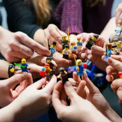 Manos sostienen figuras de Lego, creando un ambiente de **actividades team building originales** y divertidas.