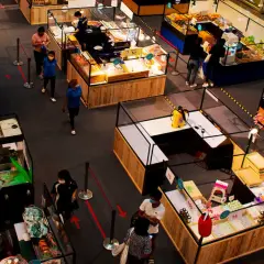 Vista aérea de una feria de emprendimiento con puestos de comida y productos diversos. Gente comprando y vendedores atendiendo.
