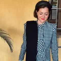 Mujer con traje de cuadros, tocado y bufanda negra. Un ejemplo de dress code elegante para un evento.