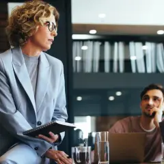 Mujer con gafas y traje gris, con cuaderno, en reunión. Podría ser parte de un curso organización de eventos gratis.