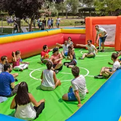 Gente disfrutando de un día familiar en empresas, sentados en un campo de fútbol inflable, riendo y jugando.