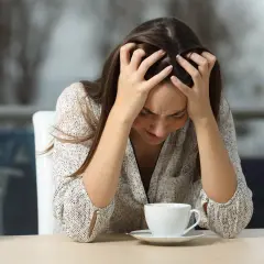 Mujer con las manos en la cabeza, mirando su taza de café, quizás porque le doy tantas vueltas a las cosas.