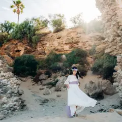 Niña con vestido blanco y corona de flores, posando en unas ruinas, un escenario perfecto para comuniones al aire libre.