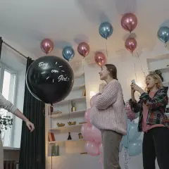 En una fiesta de revelación de género, un hombre levanta el brazo junto a un globo negro que pregunta "Boy or Girl?".