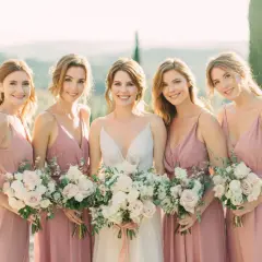 Novia sonriente con su damo de honor, todas con vestidos rosas y ramos de flores.