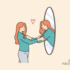 Una mujer se abraza a sí misma frente a un espejo, un símbolo de cómo trabajar la autoestima en adultos.