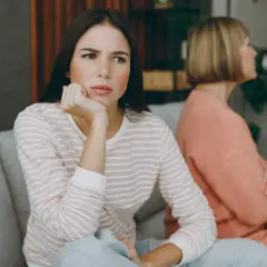 Dos mujeres sentadas en un sofá, una con expresión de aburrimiento, quizás pensando como tratar a una persona que siempre se queja.