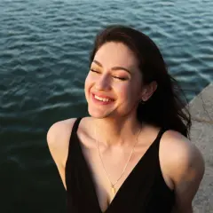 Una mujer sonríe con los ojos cerrados, sintiendo el agradecimiento por un momento de paz junto al agua.
