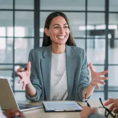 Mujer sonriente explica algo en una reunión. Podría ser un curso de mediación gratis.