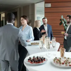 Profesionales conversan y disfrutan de canapés y bebidas en un evento corporativo.