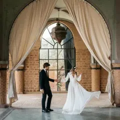 Novios bailan en un salón con arcos y cortinas, celebrando que las bodas son a los 10 años.