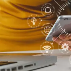 Persona usando un móvil y portátil con iconos de analítica digital superpuestos.