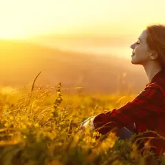 Mujer sonríe en un campo al atardecer, disfrutando de la paz y fortaleciendo su autoestima personal.