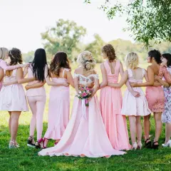Novia rodeada por sus damas de honor, todas vestidas de rosa, en un campo verde.