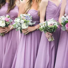 Damas de honor solteras, vestidas de lila, sostienen ramos de flores.