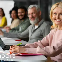 Mujeres y hombres participan en un curso formador de formadores online. Sonríen mientras aprenden en un aula moderna.