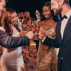 Pareja brinda con champán en una fiesta elegante. Ella luce un vestido dorado brillante, un look perfecto para una **black tie mujer**.