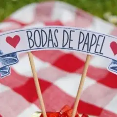 Un letrero de "Bodas de Papel" con corazones rojos, sobre un mantel de cuadros rojos y blancos.