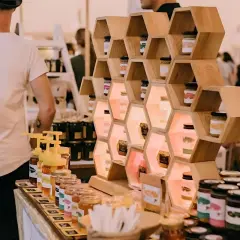 Exhibición de mieles artesanales en ferias empresariales. Tarros de miel en estanterías de madera con forma de panal, iluminados.