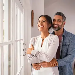 Pareja sonriente y abrazada, mirando por la ventana. Refleja cómo debe ser una relación de pareja: amor, apoyo y futuro compartido.