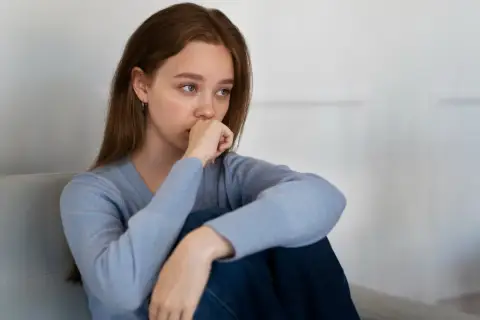 Joven con un bajón emocional, sentada en un sofá, con la mano en la boca y la mirada perdida.