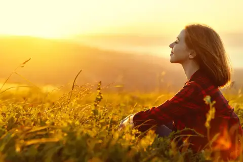 Mujer sonríe en un campo al atardecer, disfrutando de la paz y fortaleciendo su autoestima personal.
