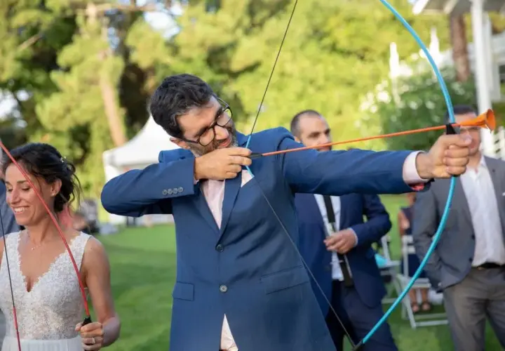 Novio con arco y flecha, parte de los juegos de bodas. La novia sonríe a su lado.