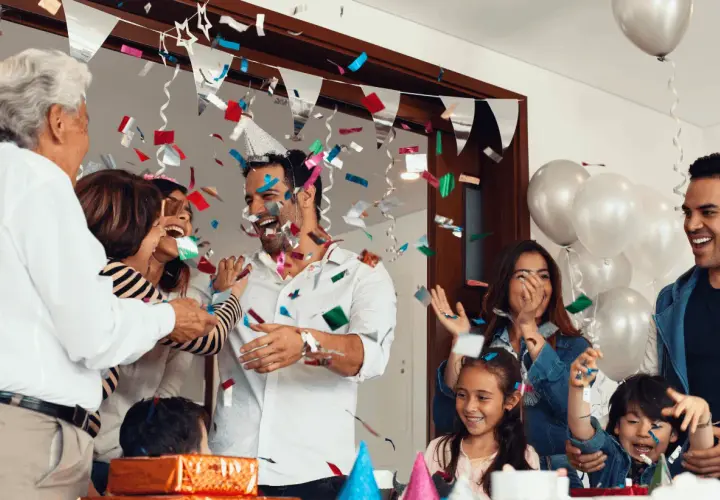 Familia celebrando fiestas sorpresa con confeti y globos. Todos ríen y se abrazan, creando un ambiente de alegría.