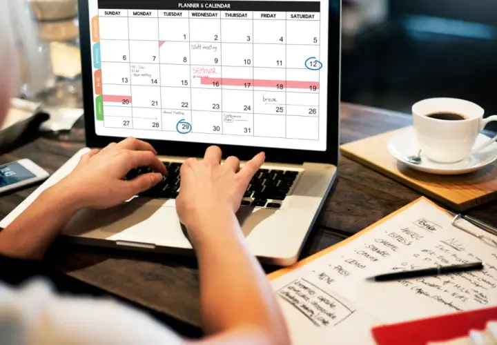 Persona organiza su **curso gestión administrativa** en un calendario digital, con una taza de café al lado.