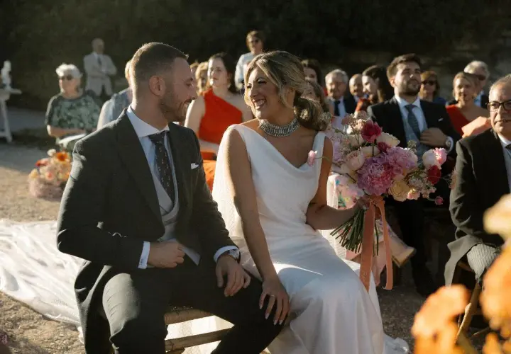 Novios sonrientes en su **matrimonio express**. Ella, radiante con vestido blanco y ramo de flores. Él, elegante de traje oscuro.
