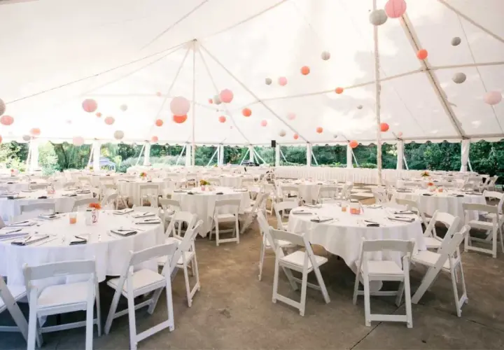 Carpa blanca con mesas redondas y sillas blancas, decorada con farolillos de colores. Un espacio ideal para **sitios de eventos**.