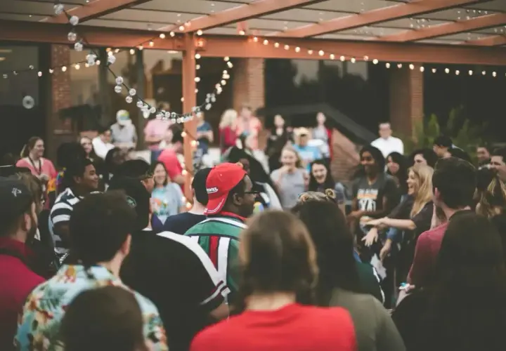 Grupo de personas disfrutando en una fiesta al aire libre, con luces decorativas. ¡Excelentes ideas para cenas de empresa!