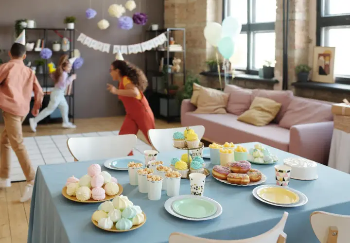 Niños corriendo en una fiesta de cumpleaños, con mesa llena de dulces y pastel. ¡Ideas de qué hacer en una fiesta!