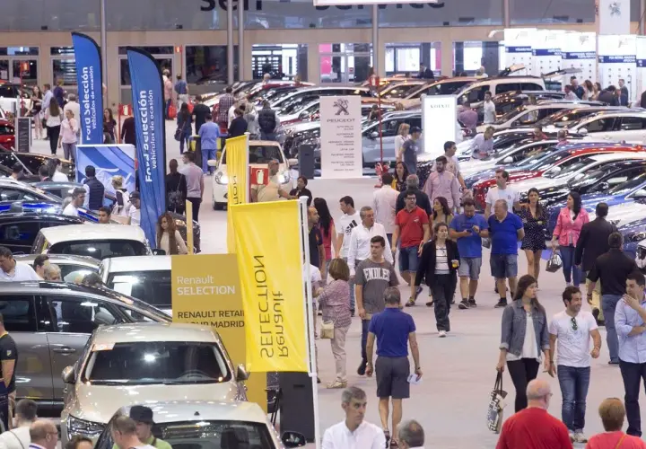 Gente paseando entre coches en una feria comercial. Banderolas de Ford y Renault anuncian vehículos de ocasión.