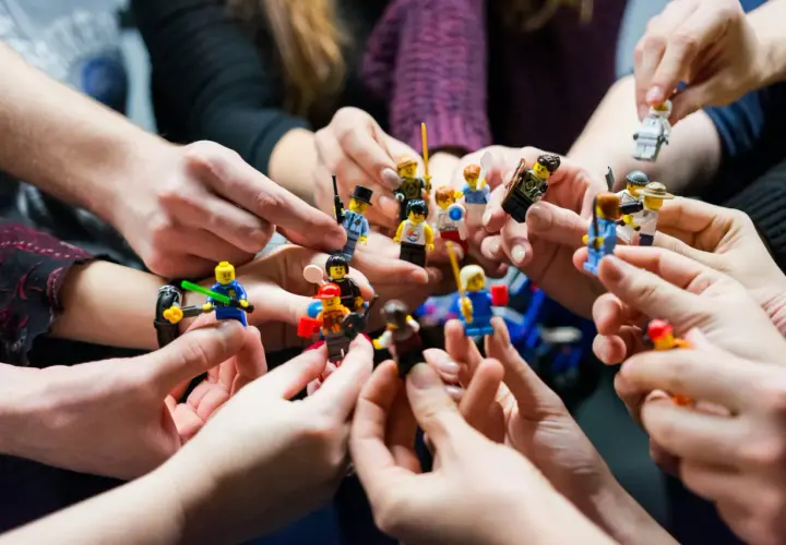 Manos sostienen figuras de Lego, creando un ambiente de **actividades team building originales** y divertidas.